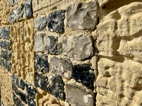 Flint and limestone checkerboard masonry close-up on the sunlit façade of Saint-Valery-sur-Somme chapelle, Picardy, France, showing weathered stone texture, tool marks and historic craftsmanship