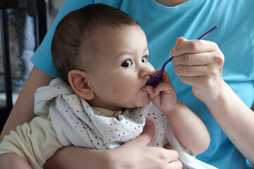 Portrait of little baby boy eating food. Baby with a spoon in feeding chair. Cute baby eating first...