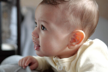 Happy newborn baby makes a funny face. Portrait of a crawling baby in his room close up