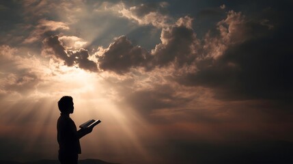 A person stands in silhouette, holding a book open and bathed in the light of a dramatic sunset.