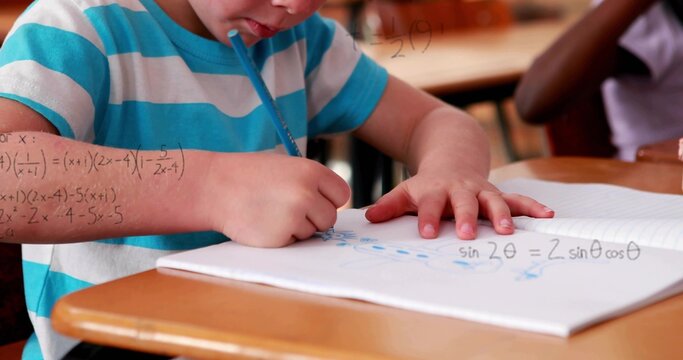 Writing student in turquoise tee leaning on spiral notebook in classroom, solving math with pencil