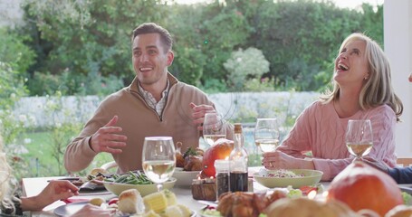 Gesturing diners in tan pullover and pink sweater sharing meal at garden table with wine bottle