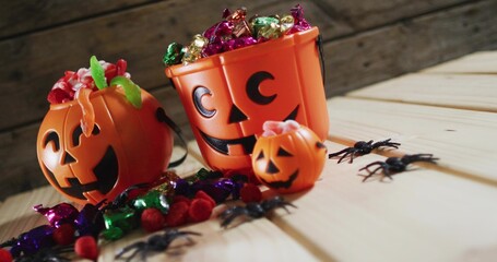 Displaying three orange jack-o'-lantern buckets on light wooden table with foil chocolates, spiders