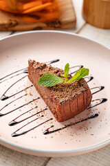 Slice of rich chocolate cheesecake garnished with mint leaves and chocolate syrup served on pink plate