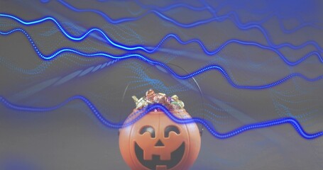 Sitting orange plastic jack-o'-lantern bucket holding wrapped candies on studio table, blue streaks