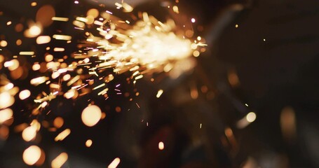 Streaming orange-yellow sparks across dark bench making embers, bokeh, smoke, source off-frame