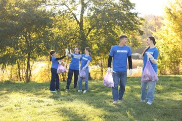 Obraz premium Group of happy volunteers with bags of trash in park