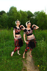Fototapeta premium Two Indian dancers in fancy dance costumes outdoors against the backdrop of nature and forestTwo Indian dancers in fancy dance costumes outdoors against the backdrop of nature and forest