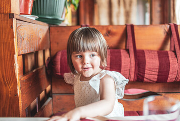 A portrait of a little girl sitting in a restaurant and waiting for a meal	