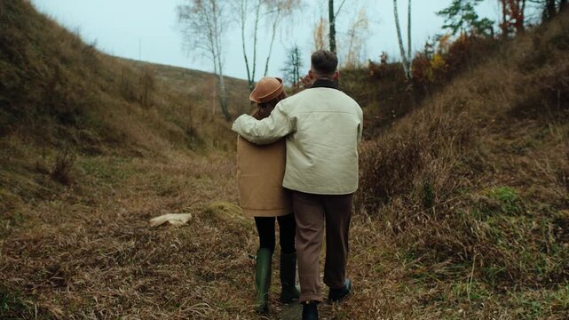 Happy young couple holding hands and walking with their pug dog in a scenic autumn ravine.