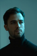Obraz premium A moody studio portrait of a man in a dark turtleneck, half his face sculpted by dramatic shadow. Creates a mysterious, thoughtful, and atmospheric ambiance. 