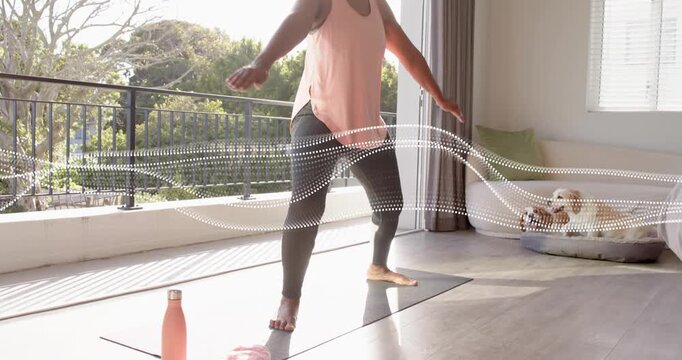 Senior woman stepping onto black yoga mat dotted wave guiding balancing pose for yoga, dog watching