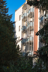 A multi-story building with red balconies and fir trees next to it. A German apartment building with balconies. Some balconies have flowers or parasols