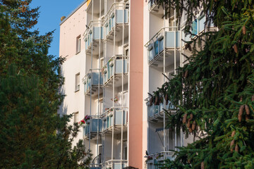 A multi-story building with red balconies and fir trees next to it. A German apartment building with balconies. Some balconies have flowers or parasols
