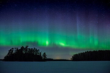 Night sky with a green aurora borealis over a frozen lake in the forests of Western Finland