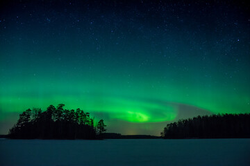 Night sky with a green aurora borealis over a frozen lake in the forests of Western Finland