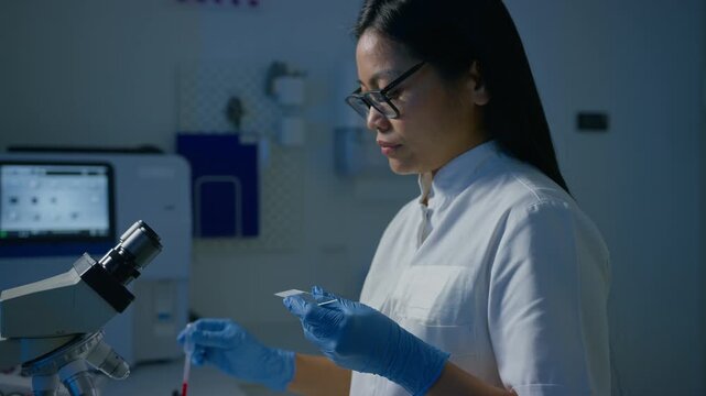 Female laboratory technician pipetting blood sample on the slide, preparing specimen for microscope examination, slow motion shot. Blood testing concept.