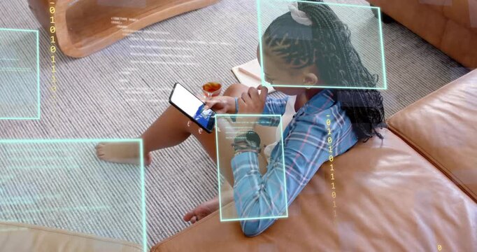 Woman sitting on floor by tan sofa tapping smartphone starting tech binary overlays checking notes