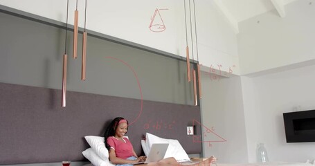 Woman typing on laptop on bed, creating red math equations covering wall while studying education - Powered by Adobe