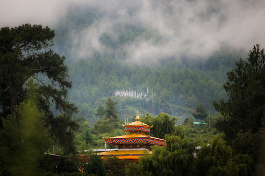 View of Kyichu Lhakhang temple nestled amidst verdant hills, shrouded in ethereal mist, a golden roof shining against the lush landscape, Paro, Bhutan.