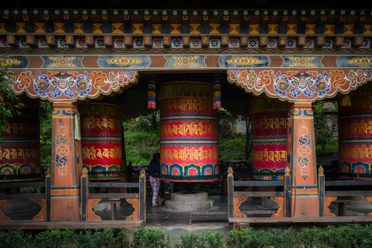 View of ornately decorated prayer wheels stand in a row, their vibrant colors and intricate designs a testament to Bhutanese artistry, Paro, Bhutan.