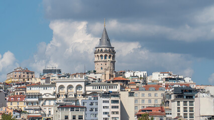 The Galata Tower rises above the surrounding buildings in Istanbul, Türkiye. The cylindrical stone tower features a conical roof and a spired top, representing significant historical architecture