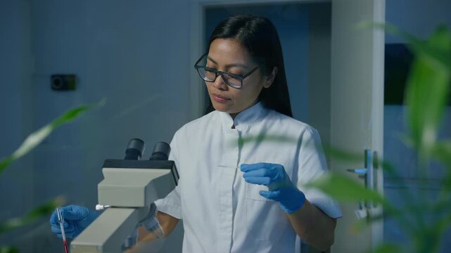 Female lab technician preparing sample for microscope examination, pipetting blood on a thin glass slide, front view. Healthcare provider concept.