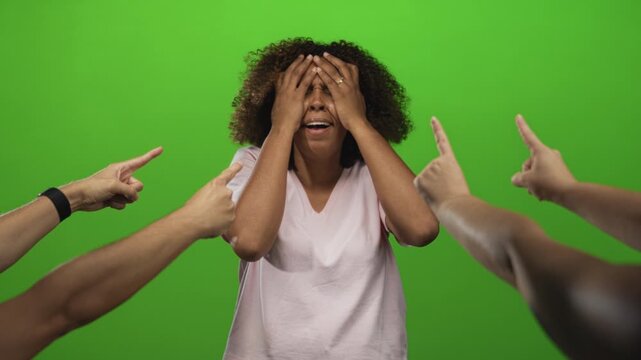 Young african american woman holding hands to forehead with distressed expression as multiple fingers point at her in a green studio; anxiety.