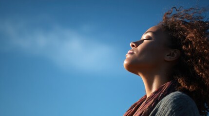 Woman breathes deeply looking up against bright blue sky background.