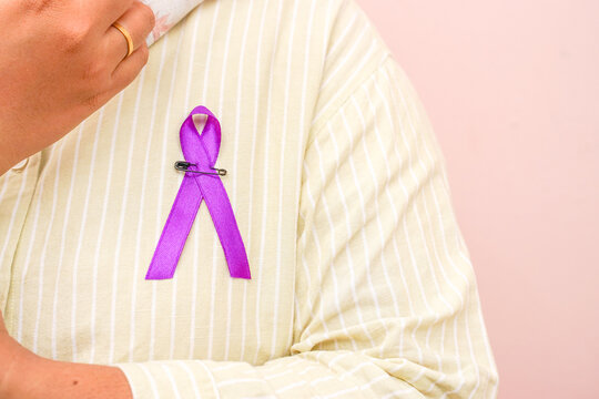 Woman in casual shirt pinned purple ribbon isolated on  pink background, for world cancer awareness and general health issues