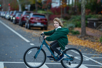 Obraz premium Fall city scene with child on bike. Kid rides bike in street. Child joyful ride bike in the city street. Child rides bike on autumn. Happy child learning to ride.