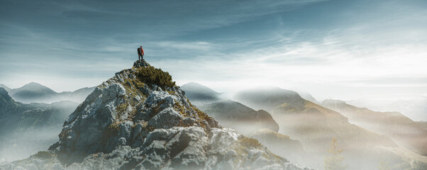 Wanderer auf einem Berggipfel schaut auf Nebelberge im Sonnenlicht