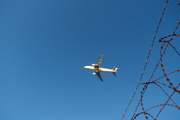 Airport barbed wire fence with plane ascending, security concept.