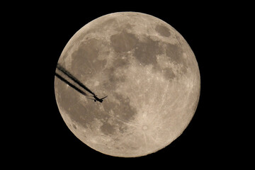 The moon and an airplane in the night sky. The plane is flying across the moon, against a black background.