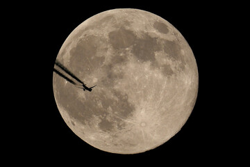 The moon and an airplane in the night sky. The plane is flying across the moon, against a black background.