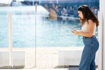 Woman with cell phone reflected in glass at the port