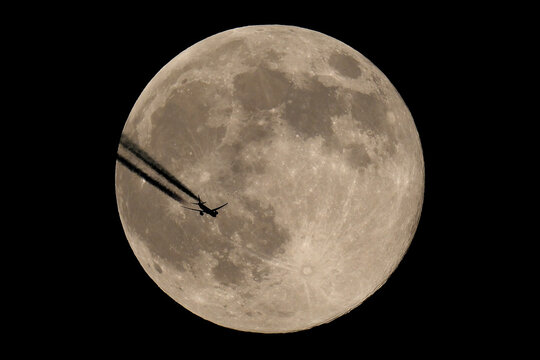 The moon and an airplane in the night sky. The plane is flying across the moon, against a black background. - Powered by Adobe