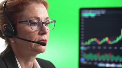 Focused female stock market trader wearing a headset and glasses analyzing financial data and charts on a computer screen with a green background actively engaged in online trading and investment dec. - Powered by Adobe