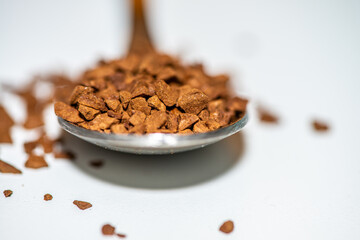 A detailed macro photo of a spoon filled with rich brown coffee grains placed against a clean white background, highlighting texture and aroma.
