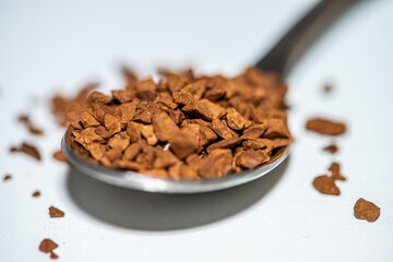A detailed macro photo of a spoon filled with rich brown coffee grains placed against a clean white background, highlighting texture and aroma.