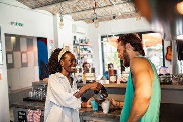 Young adults laughing as barista pours coffee at cafe