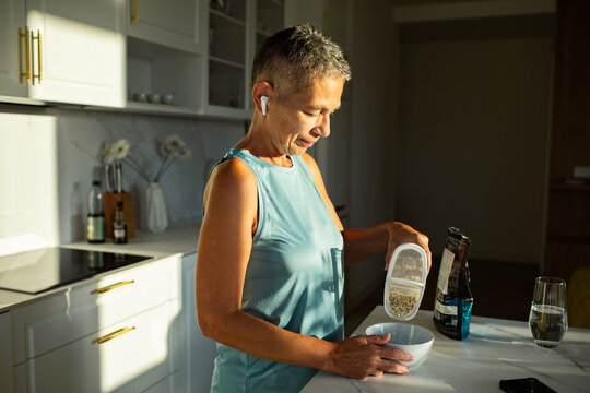 Senior woman focused on pouring granola for breakfast in modern kitchen