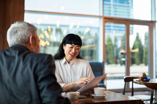Adult woman smiling while reviewing paperwork with senior man in cafe