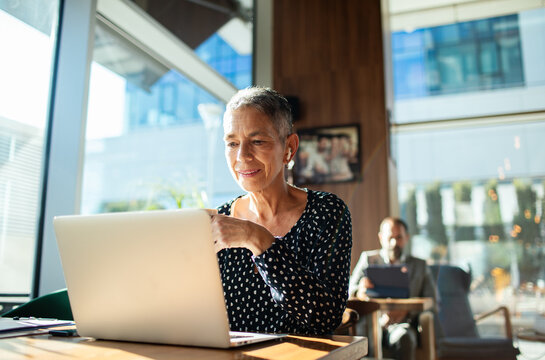 Senior woman smiling and working on laptop at cafe
