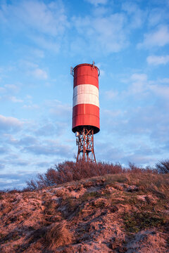 A tall red and white striped lighthouse stands against a bright blue sky. The scene evokes calm winter, rural industrial charm, and quiet everyday infrastructure.