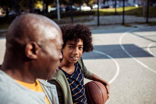 Adult father and child son talking attentively on outdoor basketball court