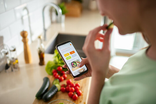 Adult woman focused on recipe app while snacking in home kitchen
