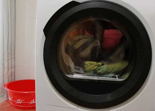 Lavadora blanca con tambor negro limpiando ropa de color en centrifugado y programa largo con cubo rojo fuera 