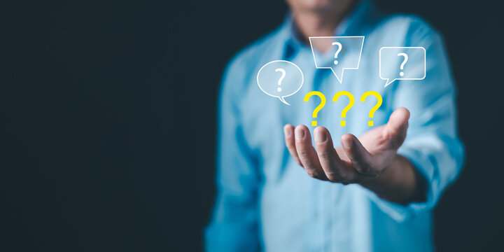 Businessman holding question marks floating above hand, symbolizing doubt, confusion, decision-making, problem solving, and brainstorming concept in business and communication.