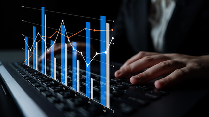 A business analyst engages with interactive data charts on a laptop keyboard, exploring financial insights and trends in a sleek office environment. Scalp